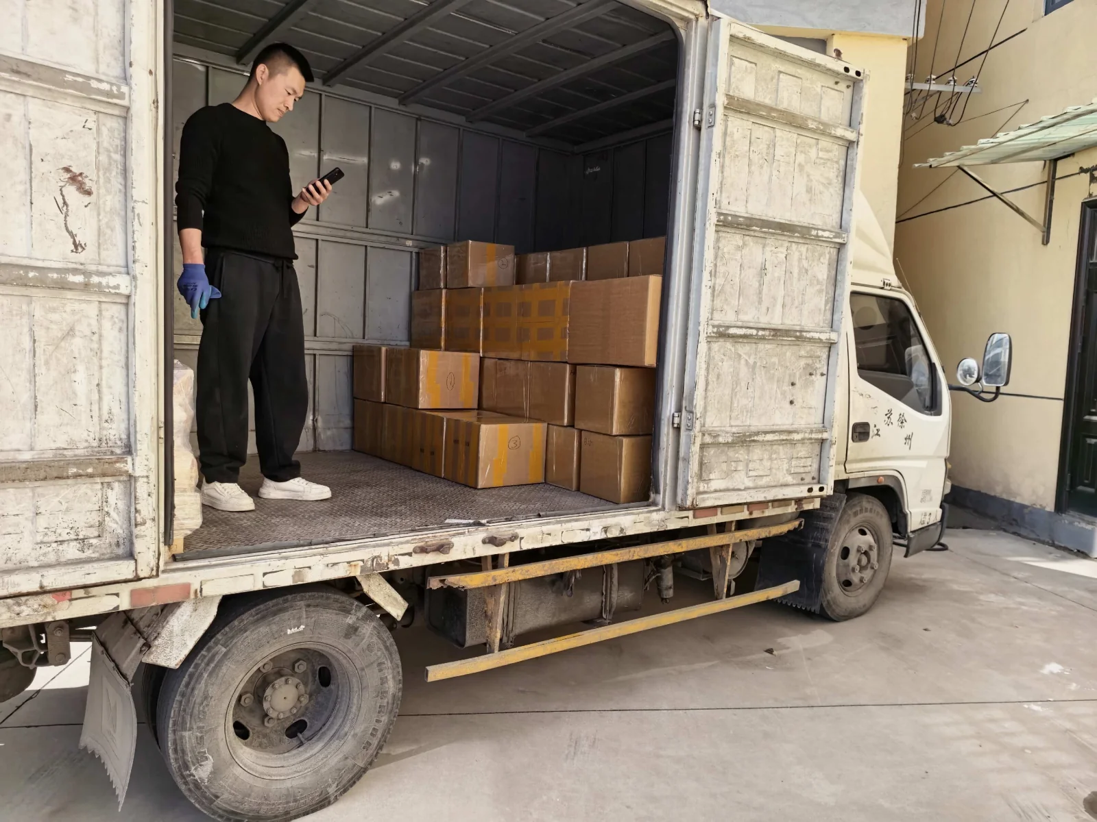 A worker in an open-sided delivery truck beside packed cartons
