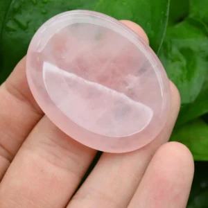 May include: A smooth, oval-shaped rose quartz crystal, polished to a high shine. The crystal is a pale pink color and is translucent. It is being held in a hand.
