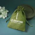 May include: A green burlap drawstring bag with white text that reads "LIZ CREATION" and "HEAL THE MIND, BODY AND SOUL". The bag is tied at the top with a matching green drawstring. The background is a dark teal color.
