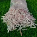May include: A plastic bag filled with many small, pink and white crystal points. The points are arranged in a random pattern and are spilling out of the bag onto a green surface.