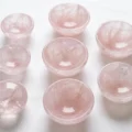 May include: Nine small, round, rose quartz bowls are arranged on a white surface. The bowls are a soft pink color and have a smooth, polished appearance. The bowls are of varying sizes and are ideal for holding small items or as decorative pieces.