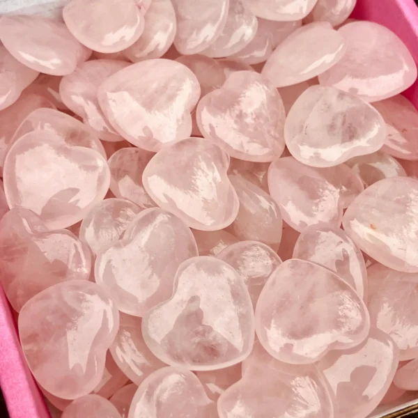 May include: A collection of polished rose quartz heart-shaped stones. The stones are a soft pink color and appear smooth and translucent. The hearts are of var May include: A collection of polished rose quartz heart-shaped stones. The stones are a soft pink color and appear smooth and translucent. The hearts are of varying sizes and are piled together.